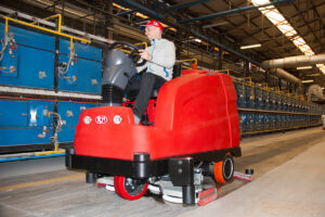 Factory Cleaning, man operating a ride-on sweeper in an industrial space.